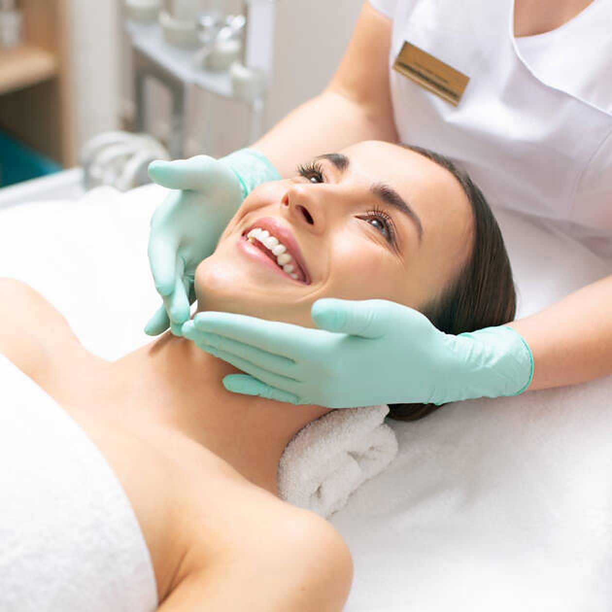 Smiling woman receiving a facial treatment from a gloved aesthetician