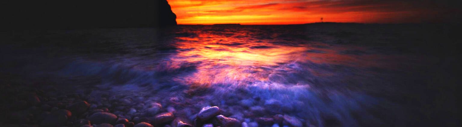Sunset over the sea with waves breaking on pebbles
