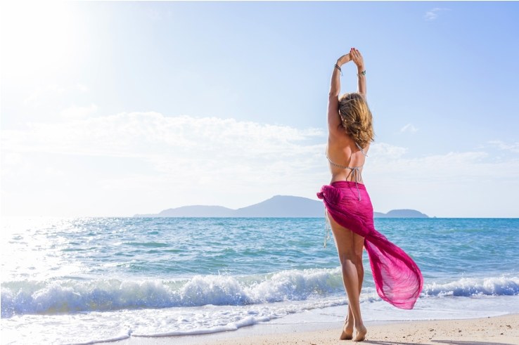 Woman in a pink sarong stretching on a sunny beach
