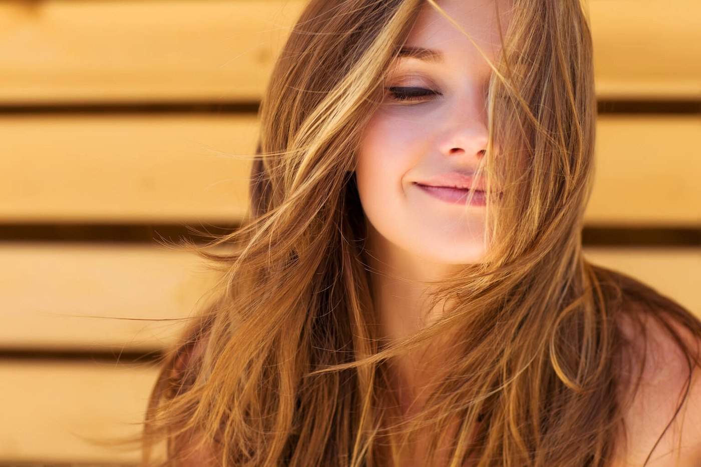 Smiling woman with windswept hair against a warm wooden background